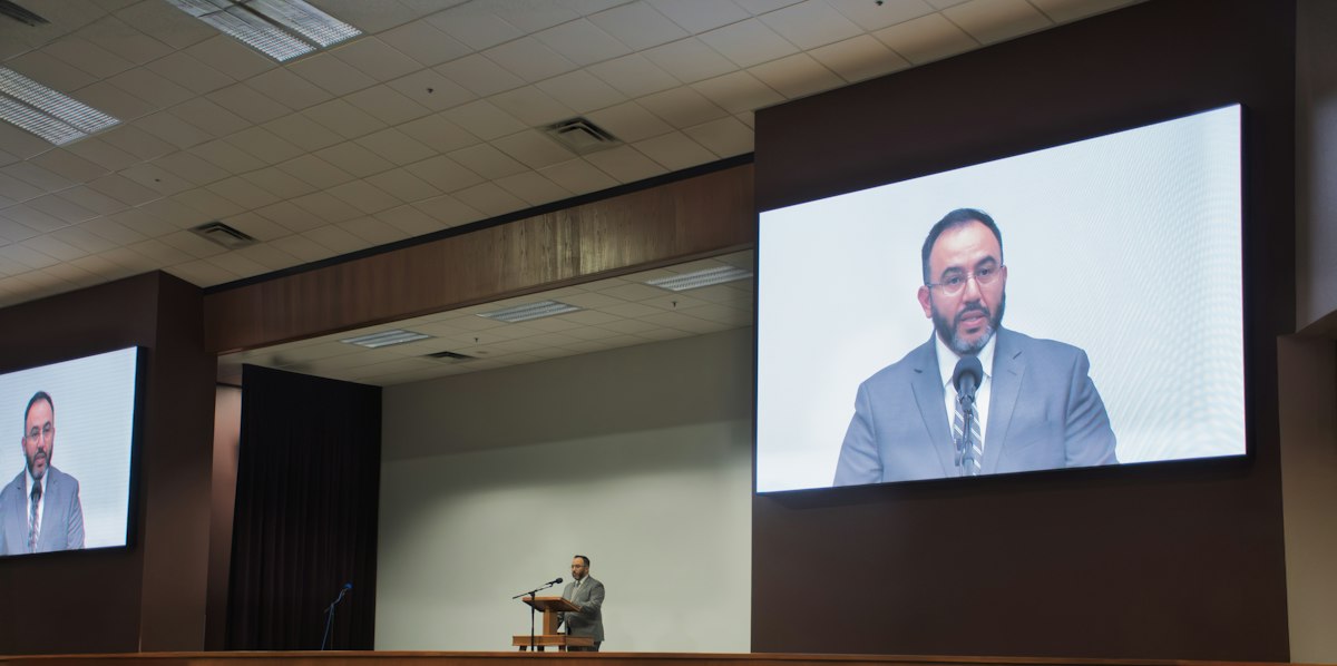 Keynote speaker at a podium with live video feed on screen Keynote speaker at a podium with live video feed on screen