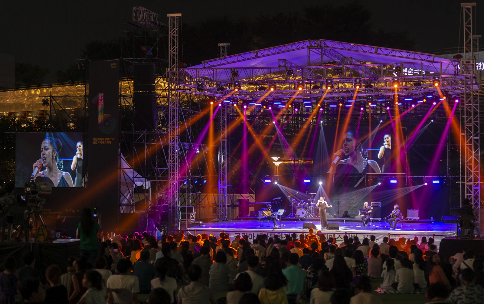 Large concert stage with truss structure, lighting and video screens in front of an audience