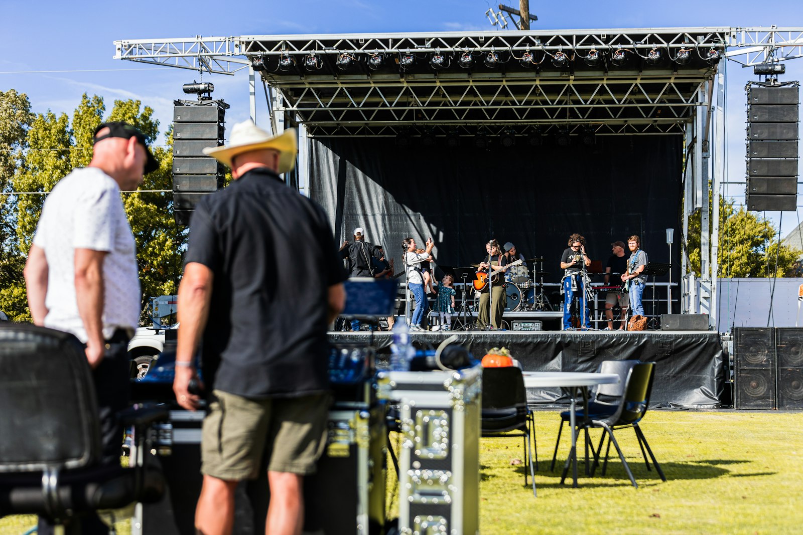 Event crew preparing equipment beside an outdoor festival stage