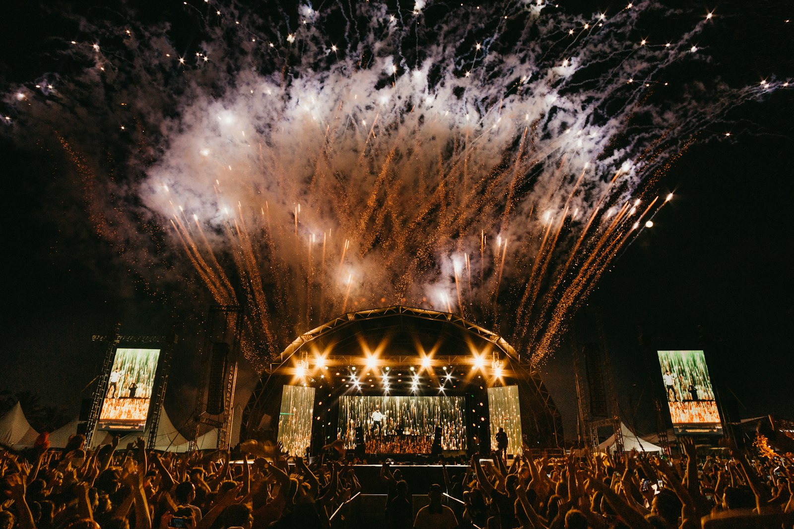 Fireworks above a festival stage as a large crowd watches the performance