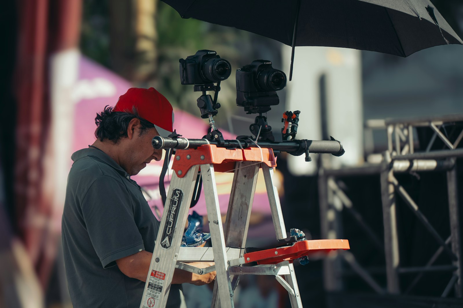 Event technician on a ladder adjusting equipment beside a stage